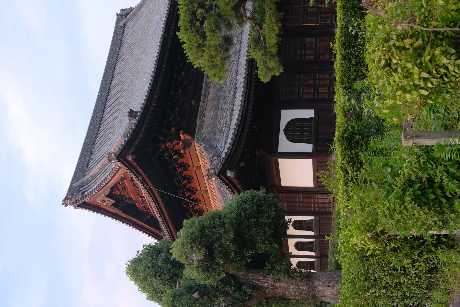 A traditional East Asian building with intricate wooden architecture and lush greenery in the foreground