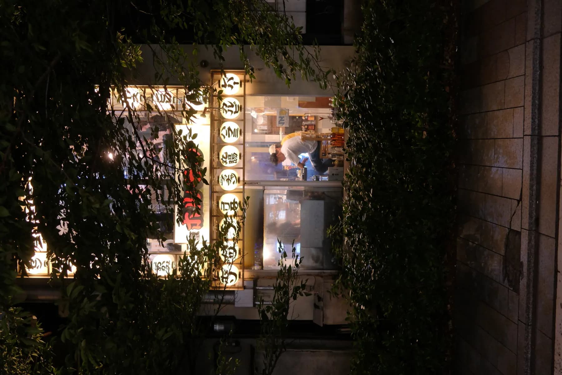 A cozy nighttime scene of a restaurant with illuminated signs and people sitting outside