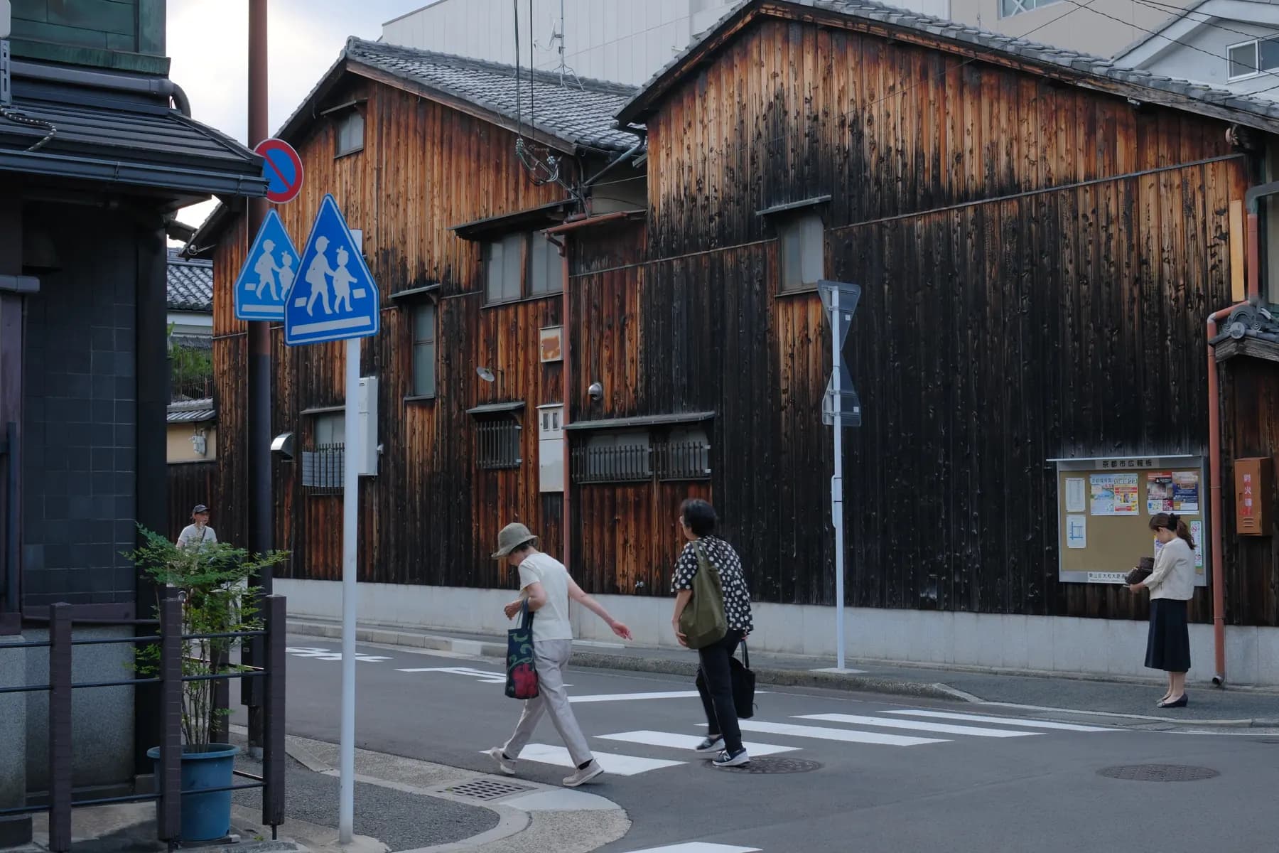 A serene urban street scene with wooden buildings, pedestrians crossing a crosswalk, and a quiet atmosphere