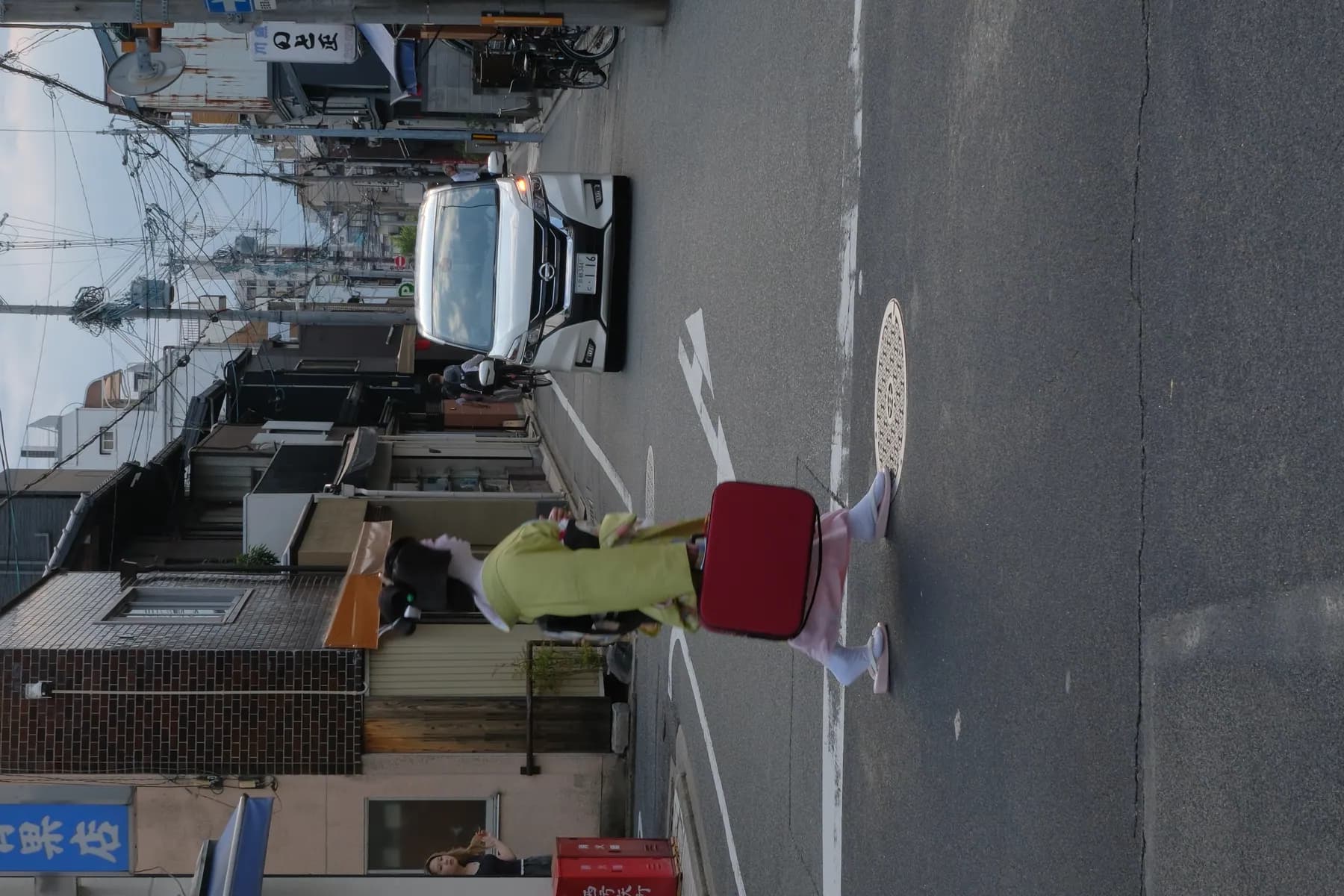 A woman in traditional Japanese attire walks across a street in an urban setting, juxtaposed against modern vehicles and buildings