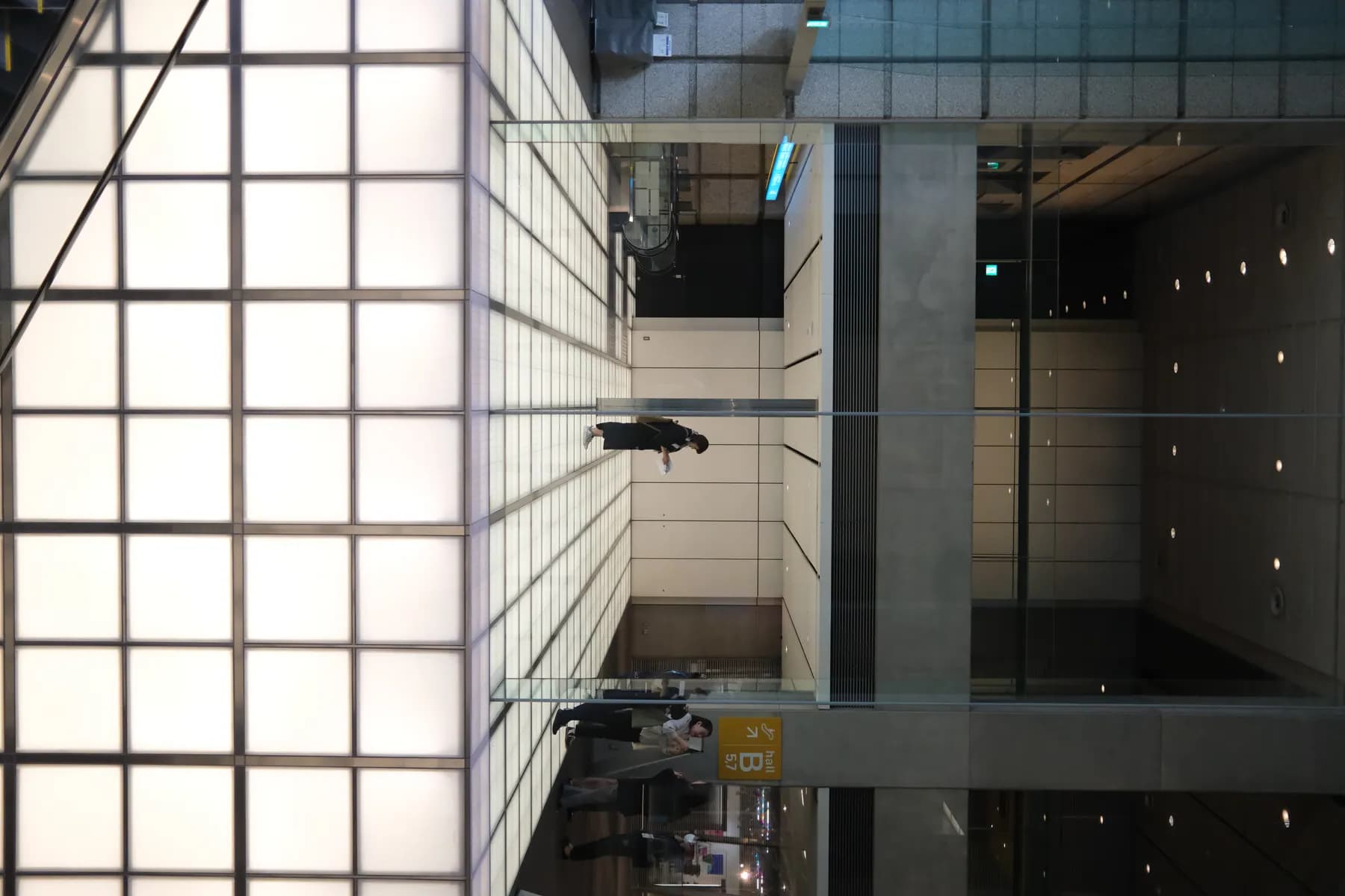 A modern indoor setting with a glass wall reflecting the interior and people walking or standing