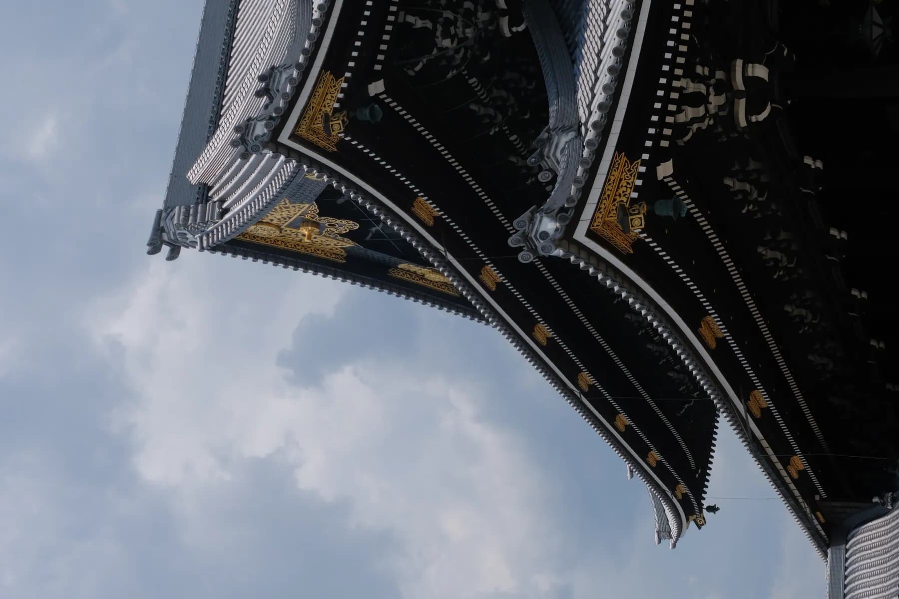 A close-up view of a traditional East Asian building's roof against a partly cloudy sky
