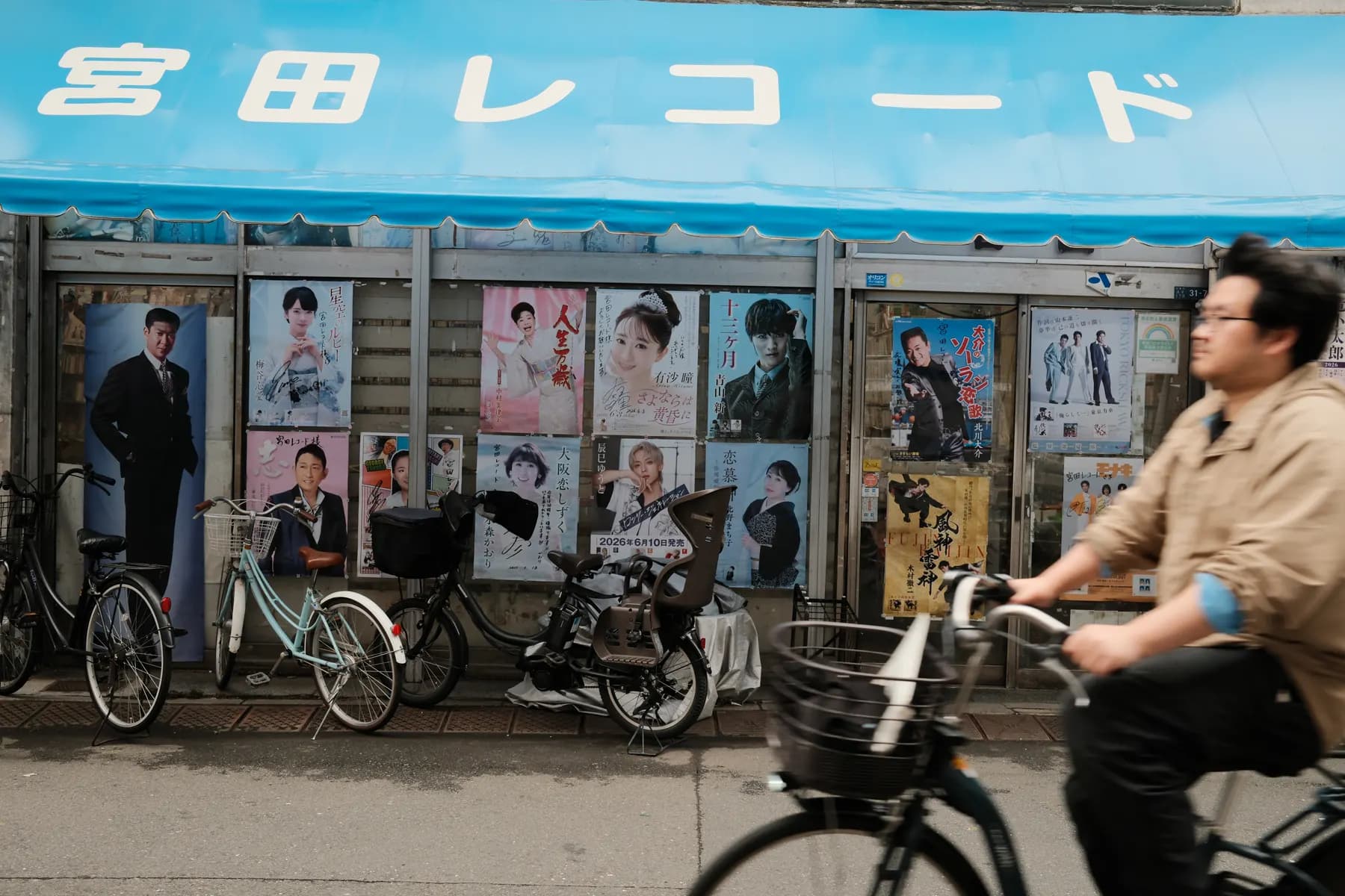 A cyclist rides past a storefront adorned with colorful posters in an urban setting