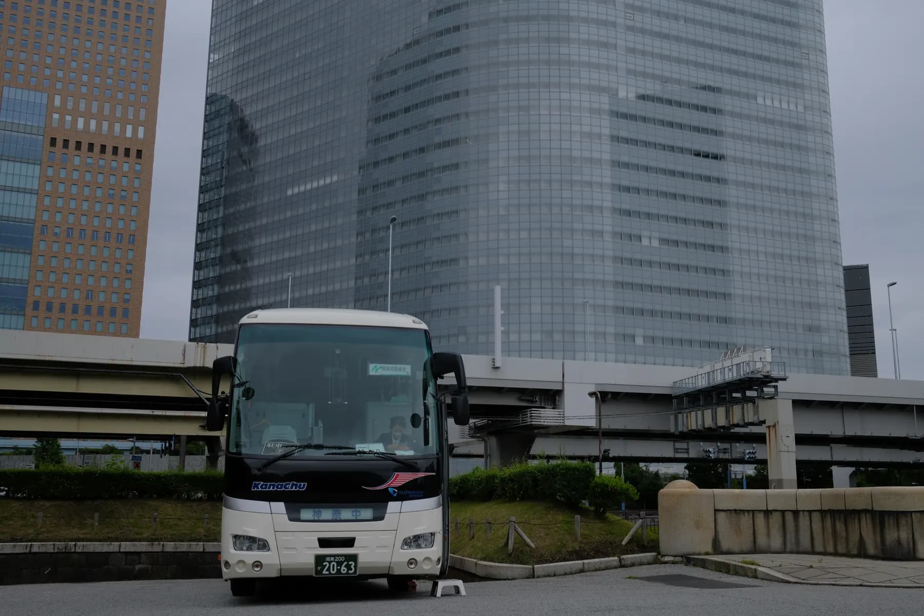 A bus is driving on a road in an urban setting with tall buildings and a bridge in the background