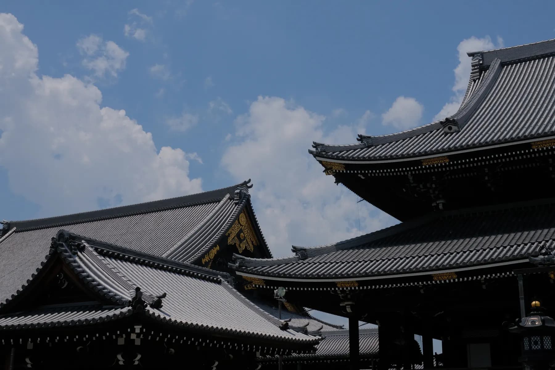 A serene view of traditional Japanese architecture under a bright blue sky dotted with fluffy white clouds