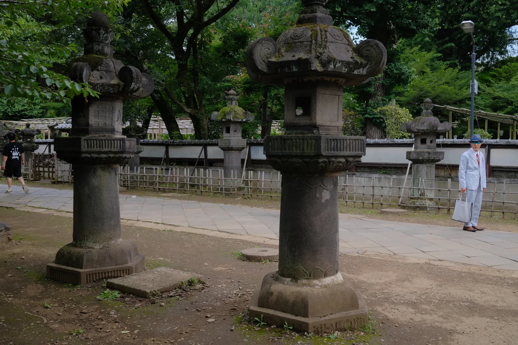 A tranquil scene featuring stone lanterns and a man in a white suit walking through a lush, mossy garden