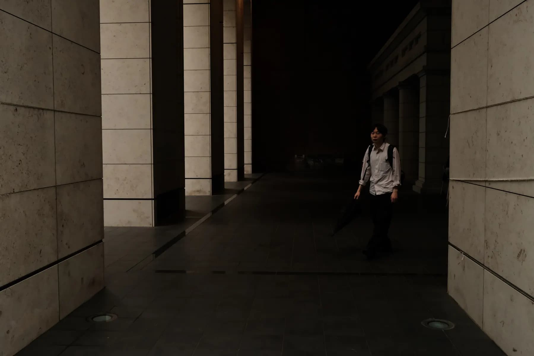 A solitary figure walks through a dimly lit urban corridor at night