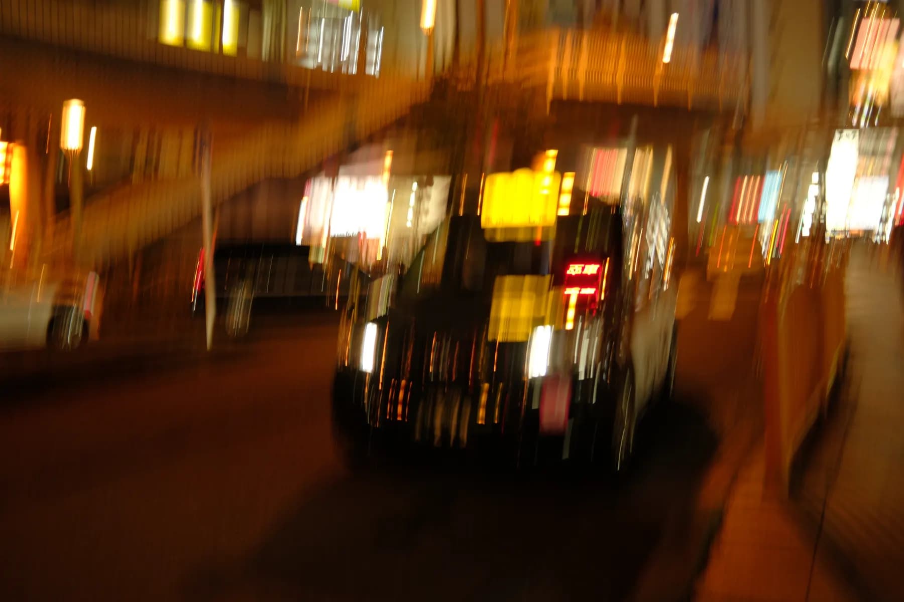 A motion-blurred image of a car on a city street at night, with buildings and streetlights in the background