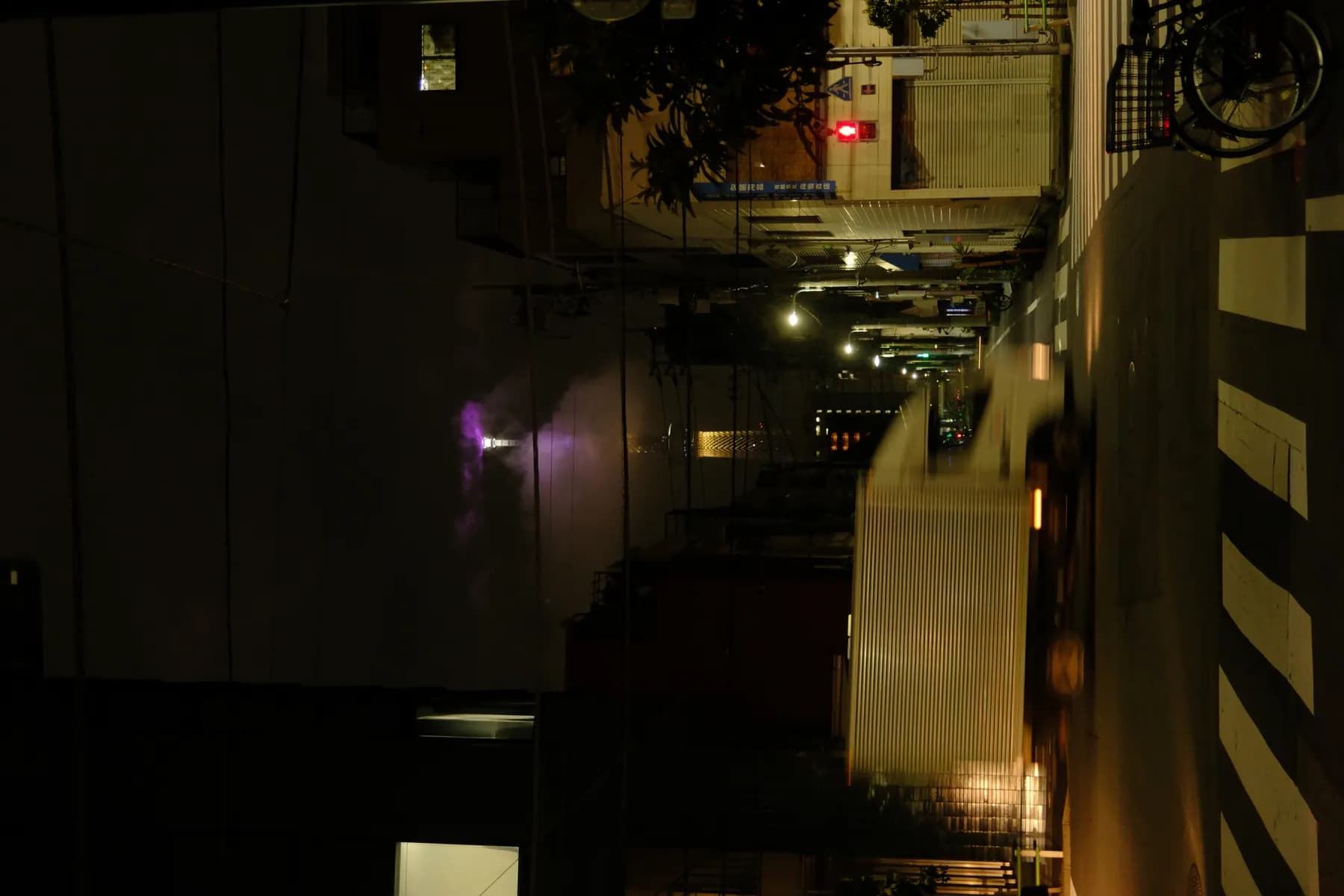 A nighttime street scene featuring a truck, buildings, and a purple smoke plume rising from a distant tower