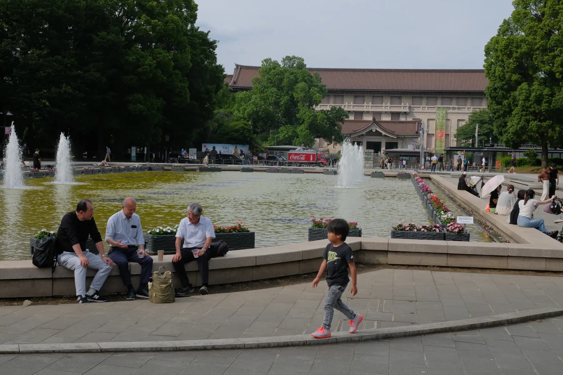 A serene scene of people relaxing near a fountain in a park with a large building in the background