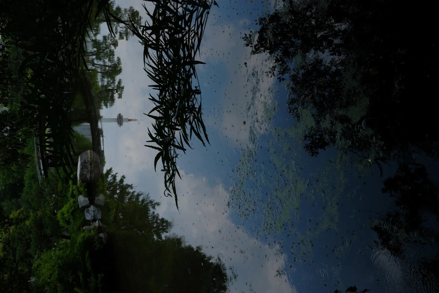 A tranquil scene of a pond reflecting the sky and a distant tower, surrounded by lush greenery and a bridge in the background