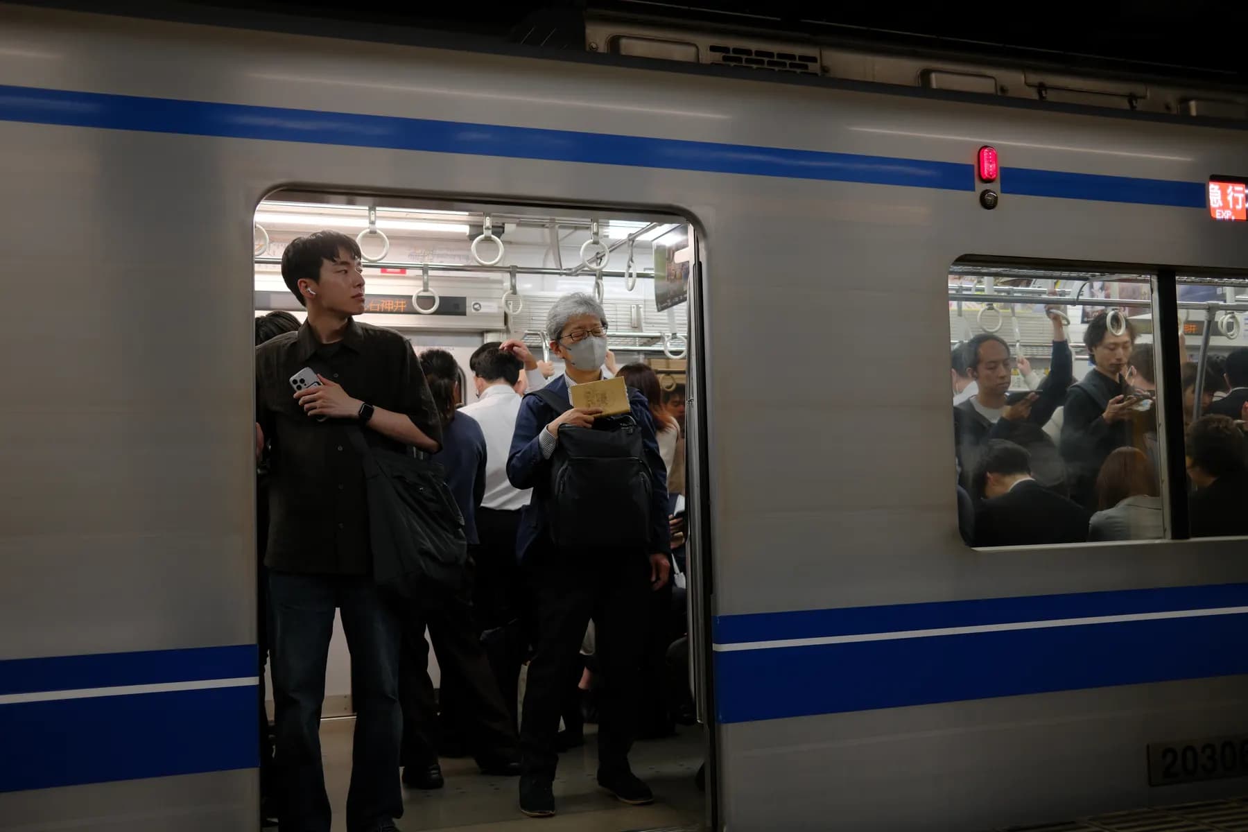 A crowded train interior with passengers standing and holding various items