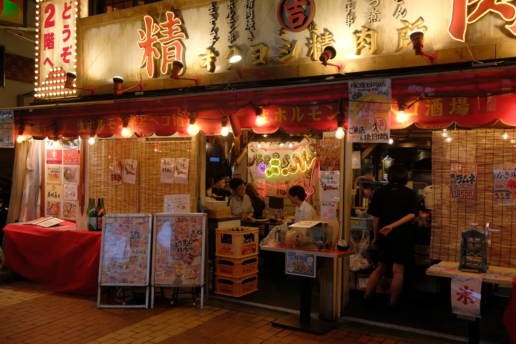 A lively street-side restaurant with colorful signage and bustling activity at night