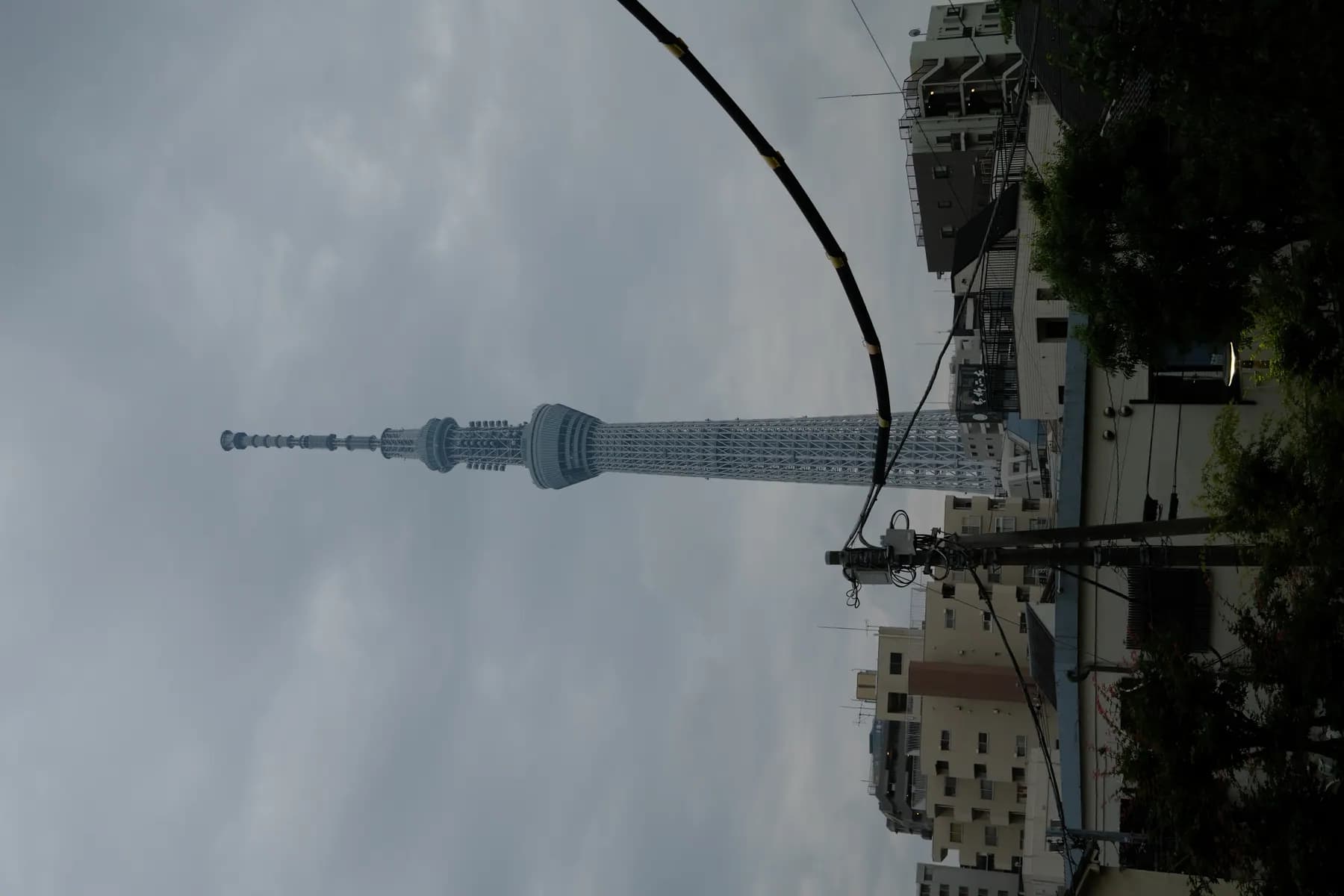 The Tokyo Skytree stands tall against a cloudy sky, surrounded by urban buildings and power lines