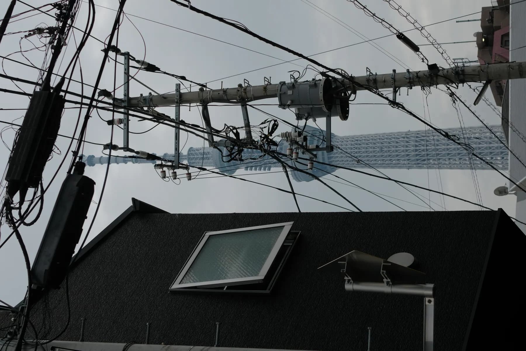 A view of the Tokyo Skytree through a cluttered urban street scene with tangled power lines and a building in the foreground
