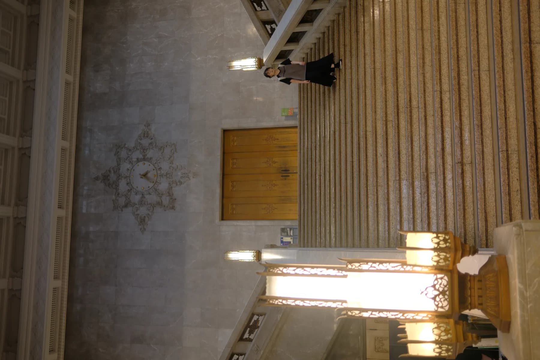 A person stands at the top of a grand staircase in a classical architectural setting