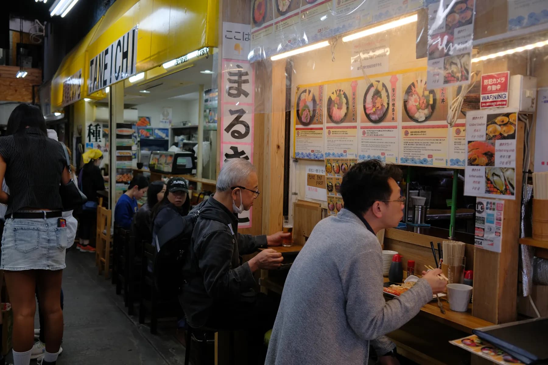 A bustling street food scene with people enjoying their meals at a counter in a brightly lit eatery