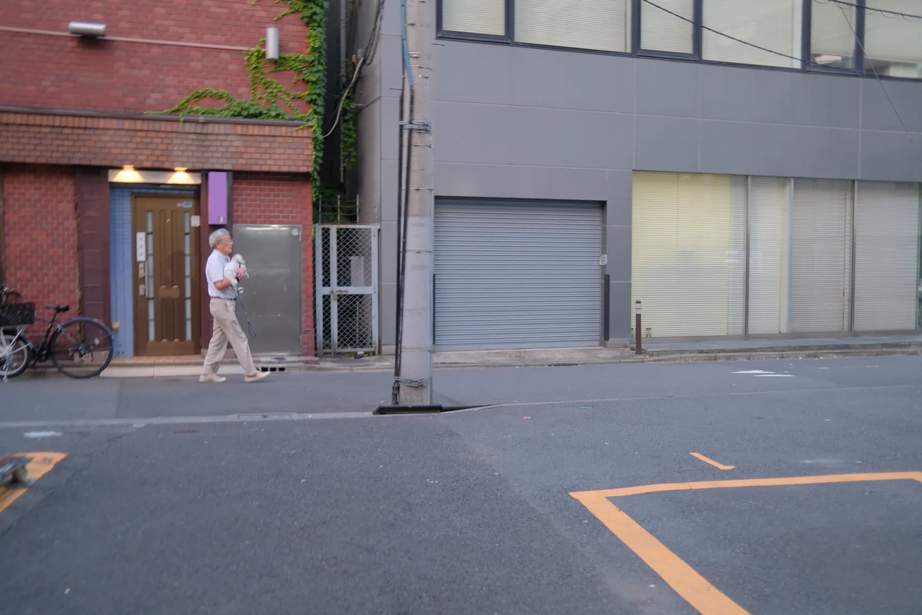 A man walks down a quiet street lined with buildings, one of which has a closed roller shutter