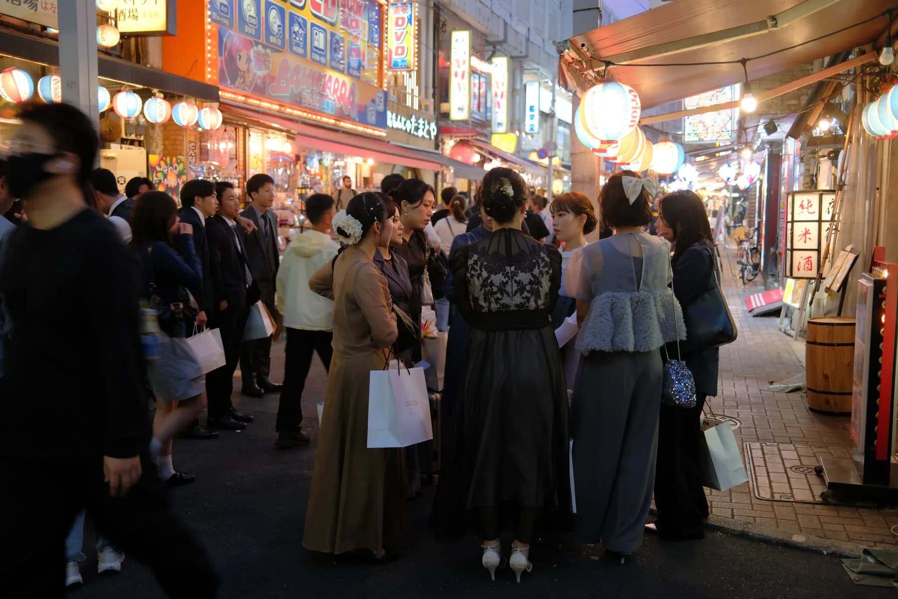 A bustling street scene at night with people dressed in formal attire, illuminated by colorful lanterns and neon signs