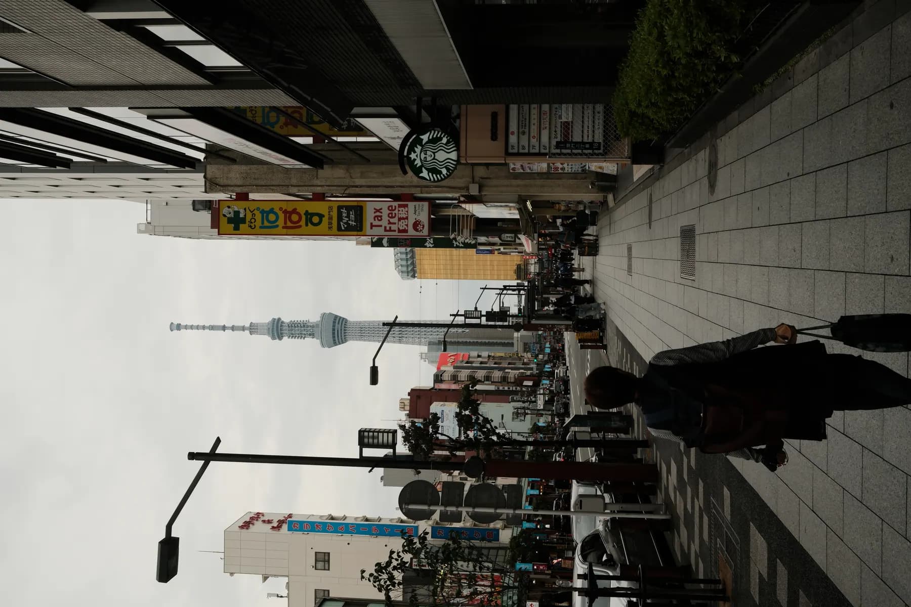 A person walks down a quiet street in an urban area, with the iconic tower in the background