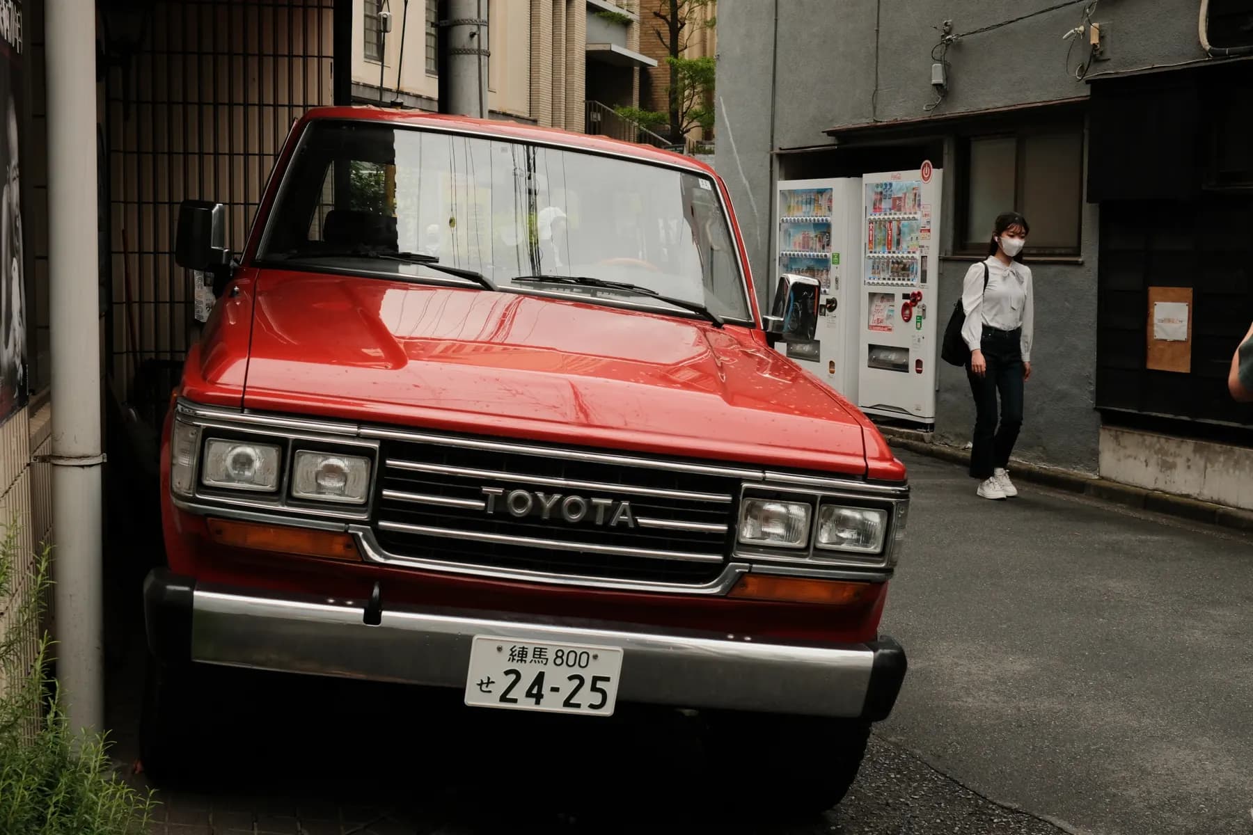 A red Toyota truck is parked on a street, with a woman walking by in the background