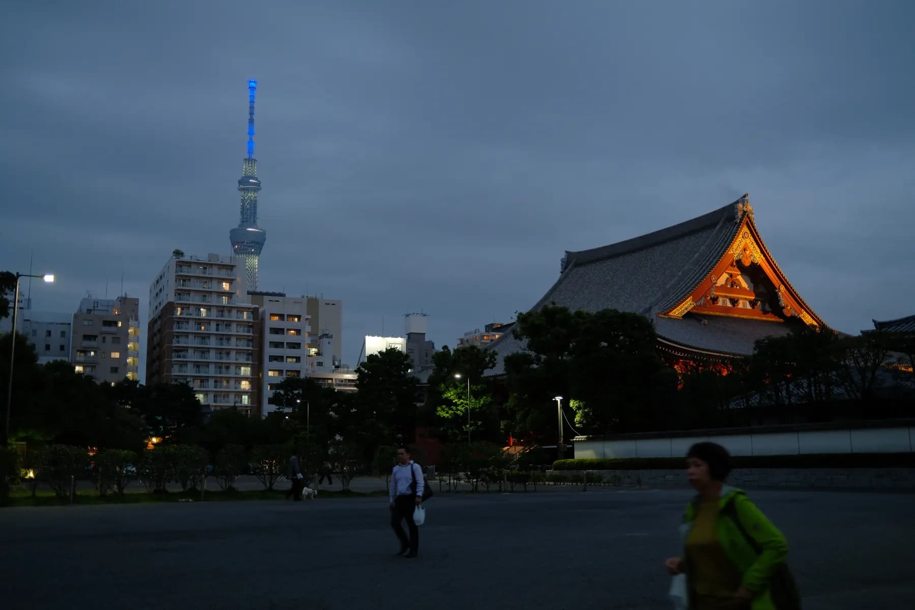 A serene sunset scene juxtaposes the modern Tokyo Skytree with a traditional Japanese temple, while people walk in the foreground