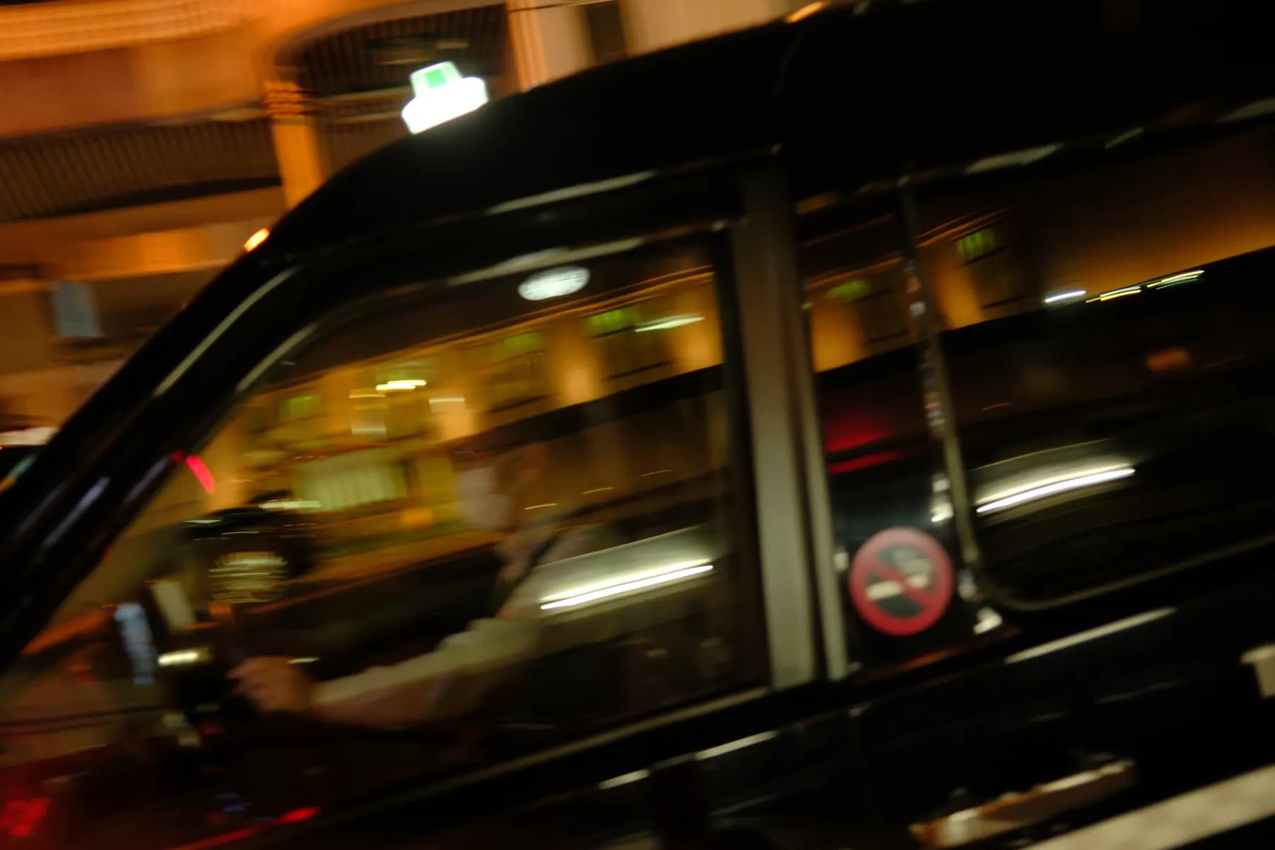A motion-blurred image of a taxi in motion at night, with a driver visible inside
