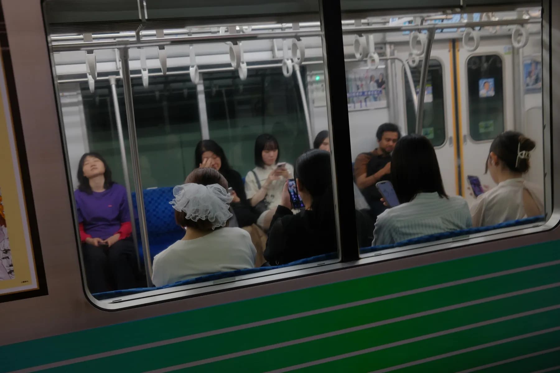 A group of people sitting on a train, some looking at their phones