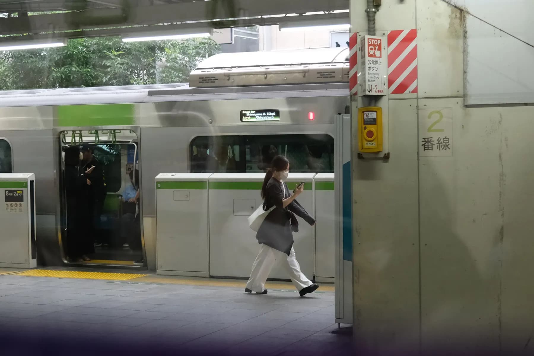 A person walks past a train at a station, with various signs and a train stop button visible