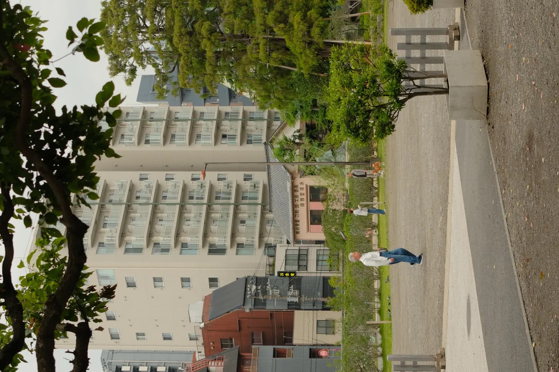 A serene urban scene with people walking and a dog in a park-like area surrounded by buildings and trees