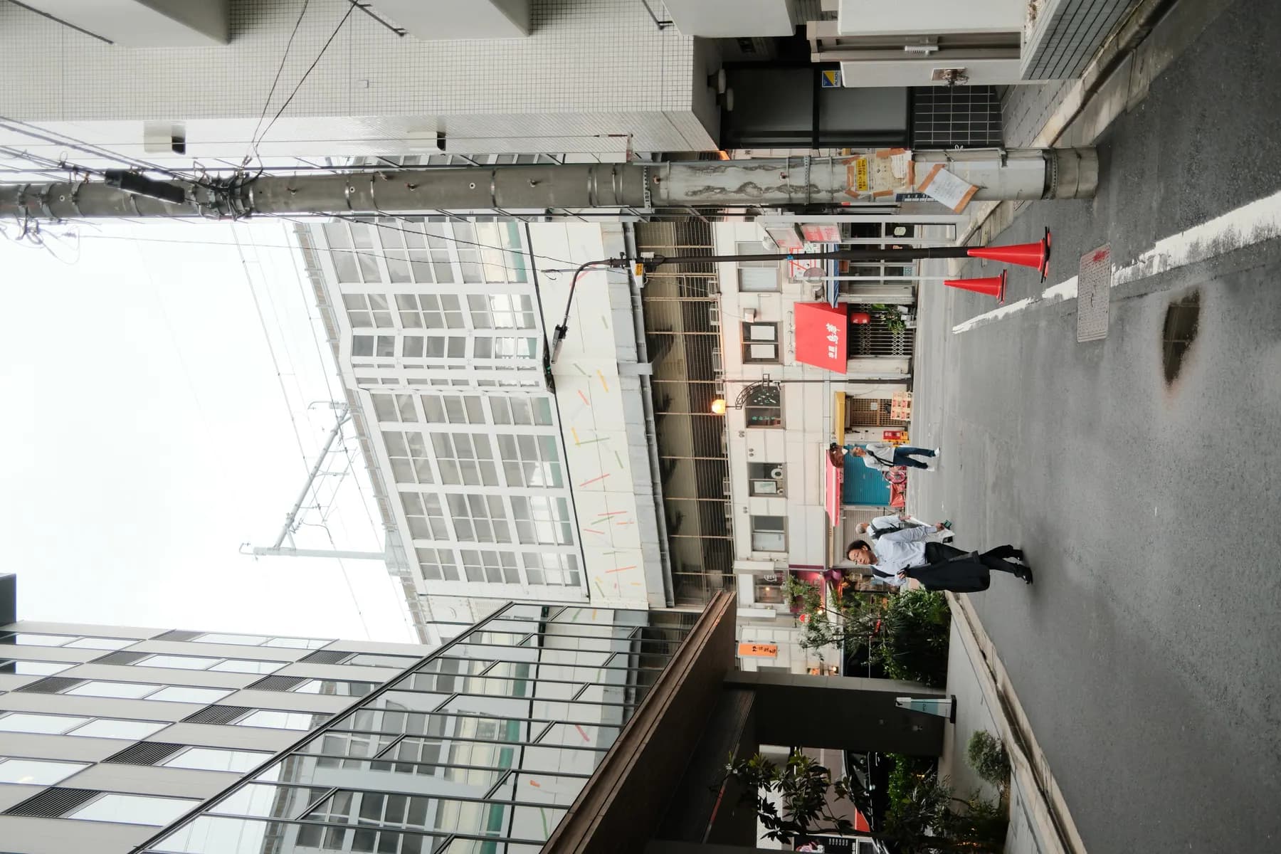 A candid street scene in an urban setting with people walking and various urban elements like buildings, street signs, and cones