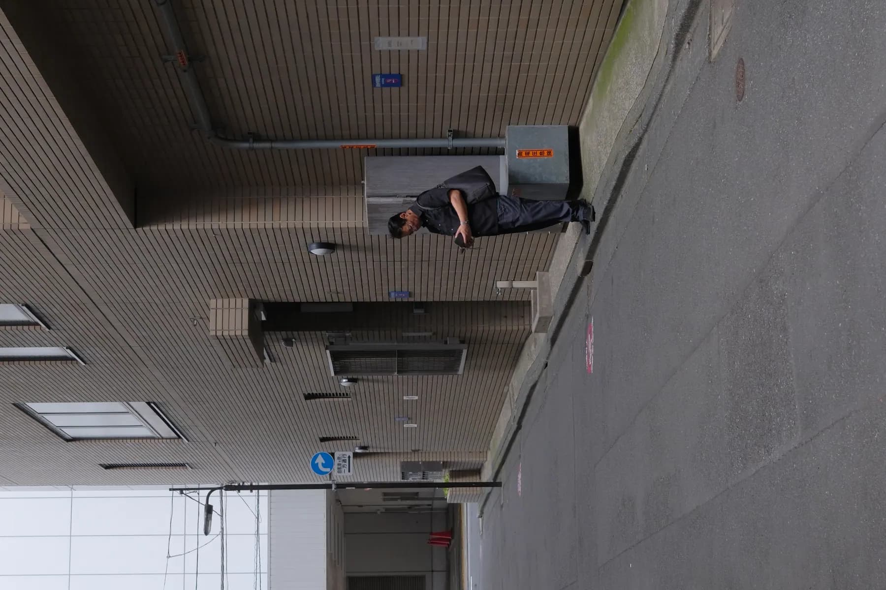 A man stands on a sidewalk, engrossed in his handheld device, in front of a brick building