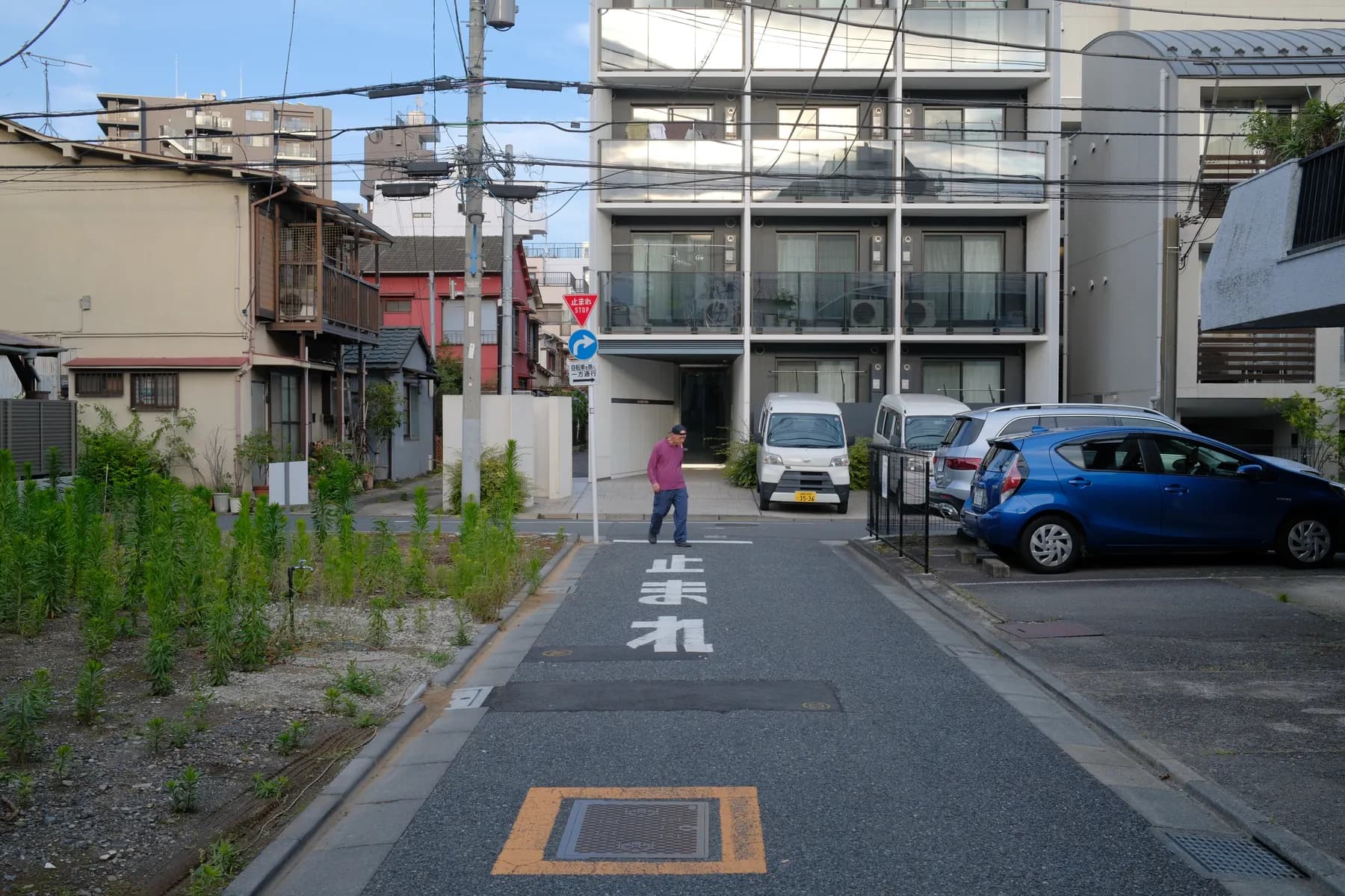 A man walks down a quiet street lined with parked cars and modern buildings in a residential area